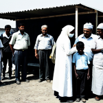 A fully clothed, diverse group of international aid workers in modest, practical attire, distributing humanitarian supplies to a group of fully clothed children and families within a temporary, clean shelter. In the background, fully clothed journalists capture the scene with vintage film cameras and early television equipment, highlighting media's powerful role in global awareness. The atmosphere reflects compassionate assistance and the birth of international humanitarian action. The image features perfect anatomy, correct proportions, natural poses, well-formed hands, and proper finger count. Professional photography, high quality, safe for work, appropriate content, family-friendly, fully clothed.